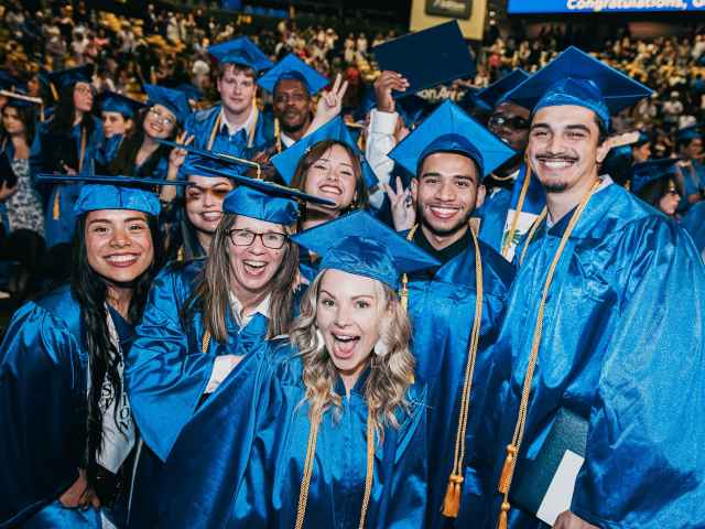 Students in graduation regalia smile and pose for photo.