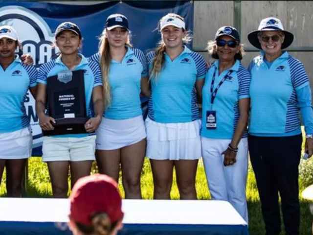 Christa Teno stands at the very right of her team. Everyone smiles at the camera.