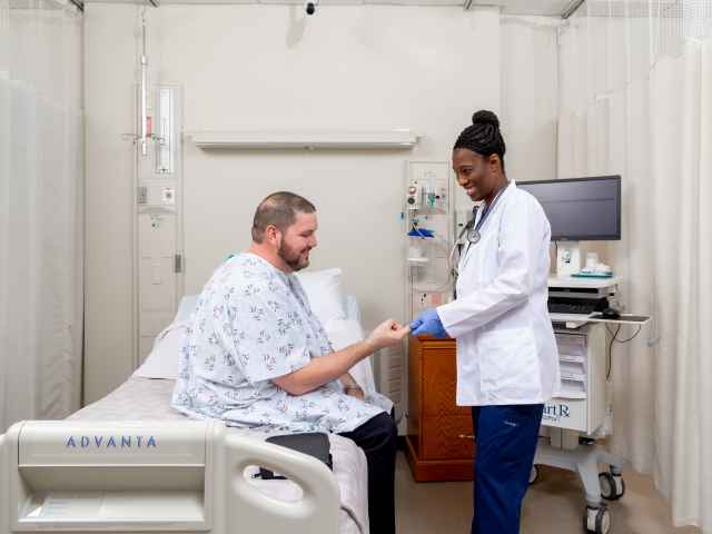 A nurse helps a patient sitting on a hospital bed.