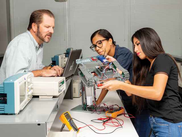 Students at Seminole State College handle a robot while a professor looks on. Seminole State is now offering coursework in mechatronics and robotics.
