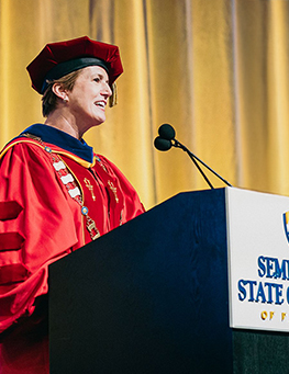 Dr. Georgia Lorenz in Graduation regalia speaks at a podium during graduation.