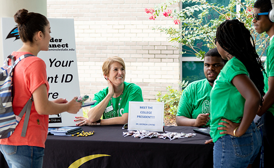 A student meets Dr. Georgia Lorenz at an outdoor welcome table during an orientation event.