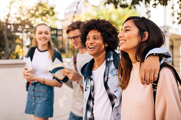 Group of students walking together outdoors, laughing and carrying books.