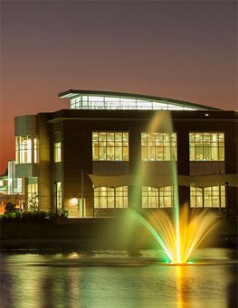 Campus building illuminated at dusk with a colorful fountain in the foreground.