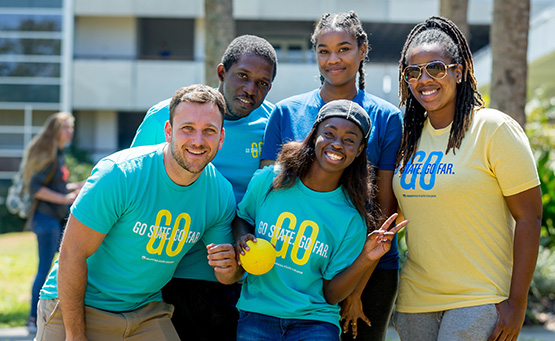 Group of students wearing “Go State. Go Far.” shirts posing together outdoors and smiling.