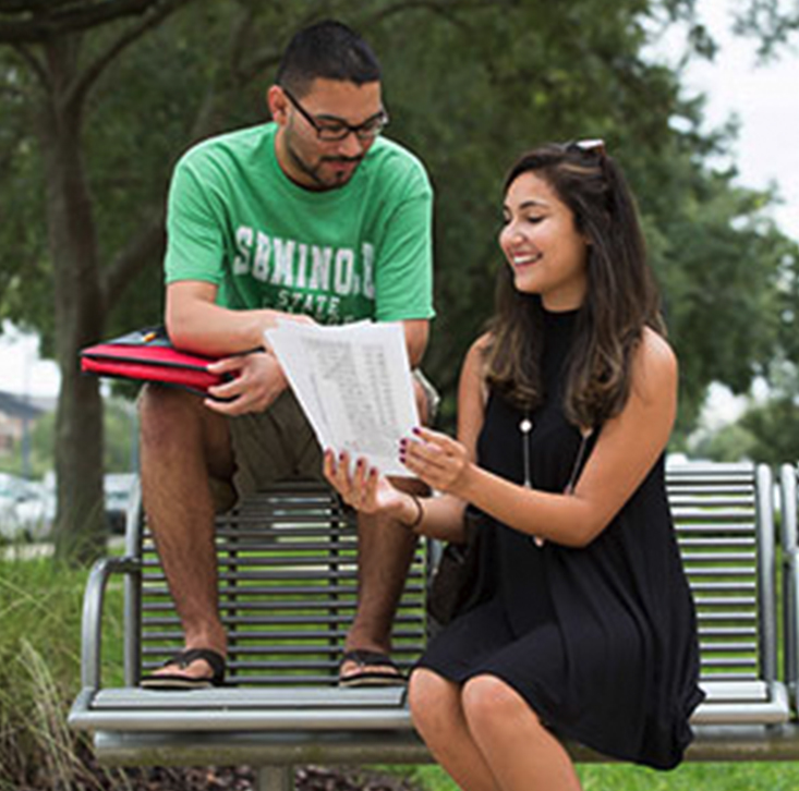 Two students sitting on an outdoor bench reviewing class notes together.