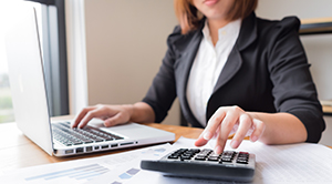 A lady typing on a laptop keyboard and a calculator at a desk in an office