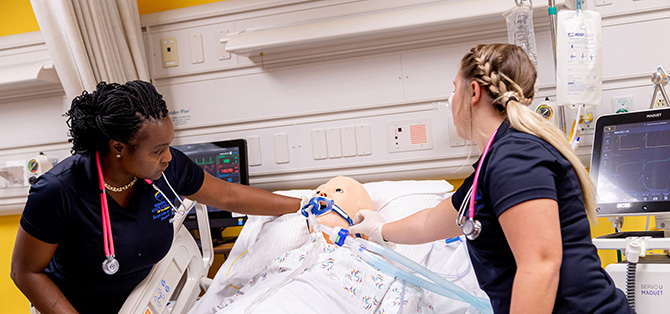 Two respiratory care students adjusting IV and respiratory equipment on a simulation manikin in a clinical lab.