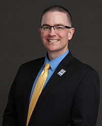 Dr. Tom Hoke wearing a dark suit with yellow tie.