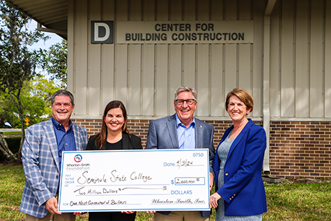 Dr. Lorenz and Wharton-Smith donors holding a large white $2million dollar check outside of the Wharton-Smith Construction building on the Sanford/Lake Mary Campus