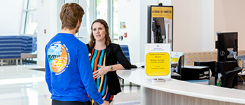 A female SSC employee talking to a SSC male student at the Information Desk in the Sanford/Lake Mary Student Union building 