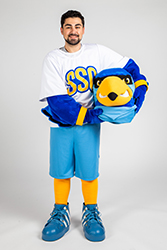 'A person standing the full Rally suit and holding the mascot head on their side.