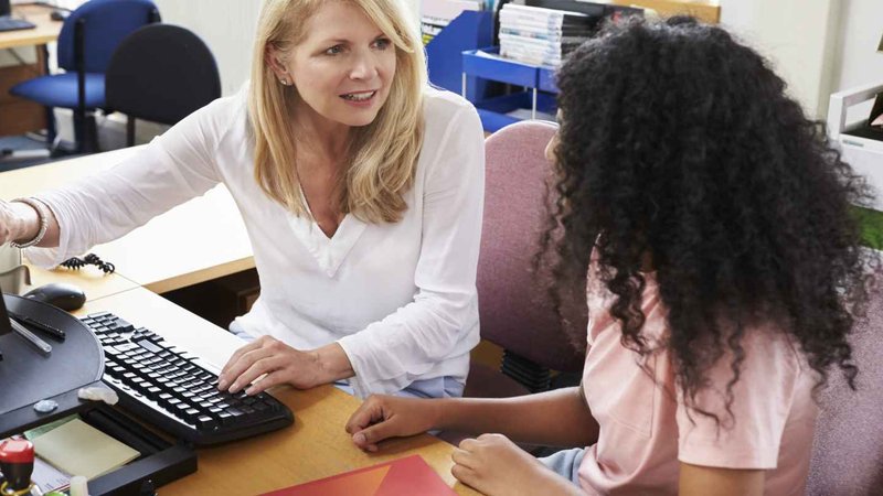 A staff member helps a student at a computer.