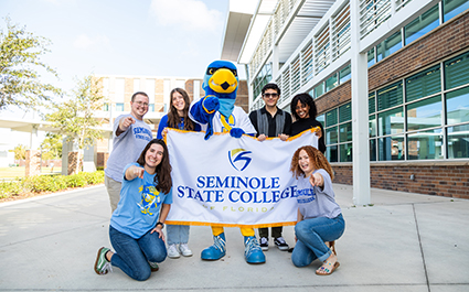 Rally standing with a group of students, holding a Seminole State College of Florida banner, and pointing at the camera.